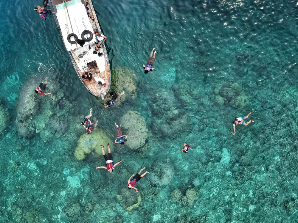 Aerial view of people snorkeling near a boat in clear turquoise water over coral reefs.